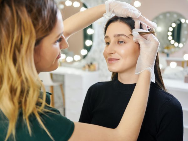 Beauty specialist plucking woman eyebrows with tweezers.